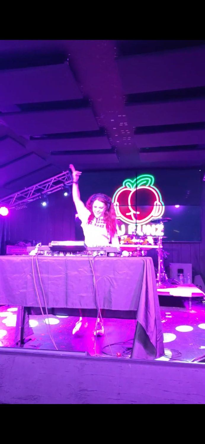 DJ Bunz performing on stage beside her lit peach neon sign